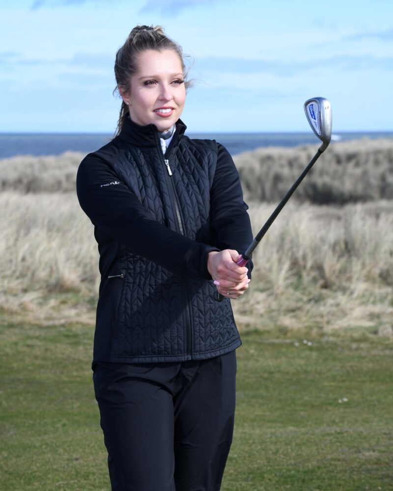 A blonde haired lady golfer wearing a black ProQuip ProFlex quilted jacket