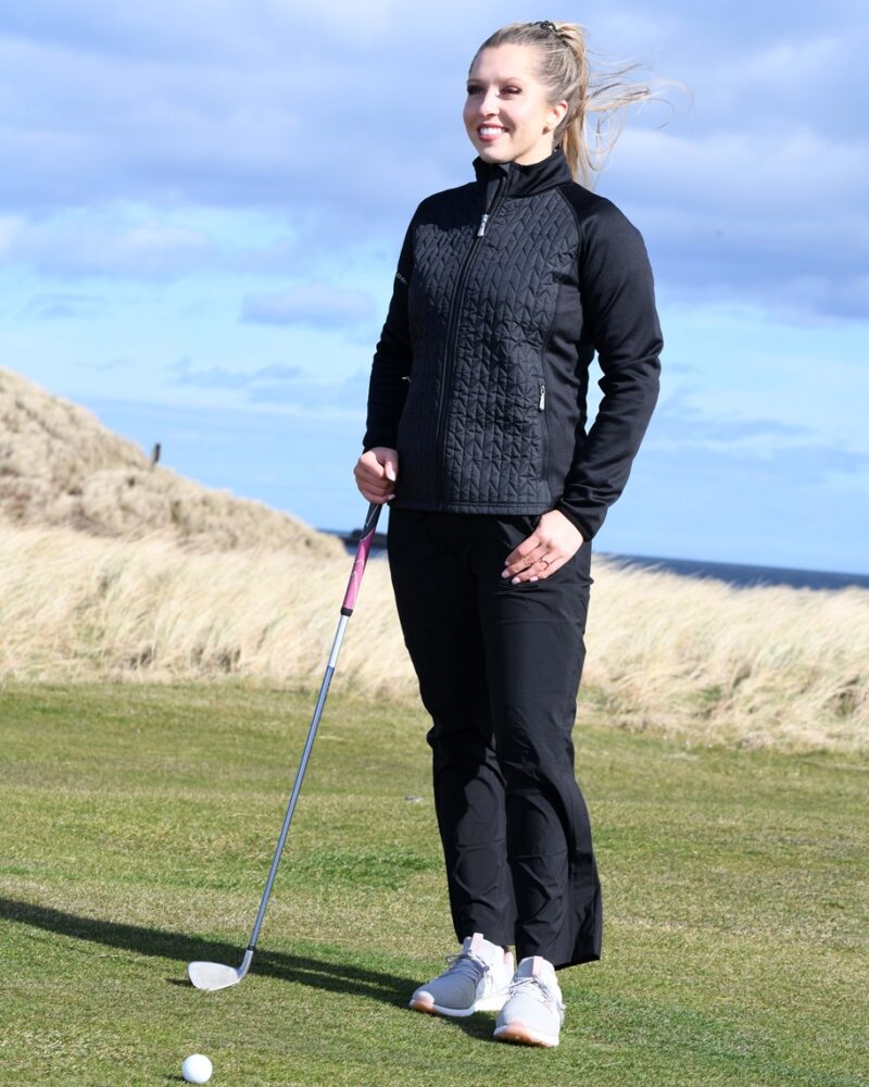 A blonde haired lady golfer wearing a black ProQuip ProFlex quilted jacket
