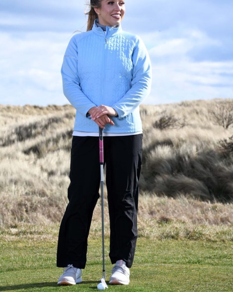 A blonde haired lady golfer wearing a blue ProQuip ProFlex quilted jacket