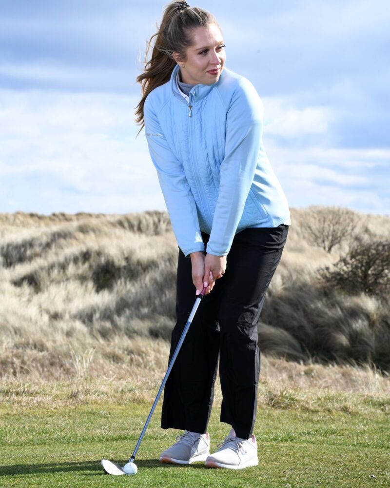 A blonde haired lady golfer wearing a blue ProQuip ProFlex quilted jacket