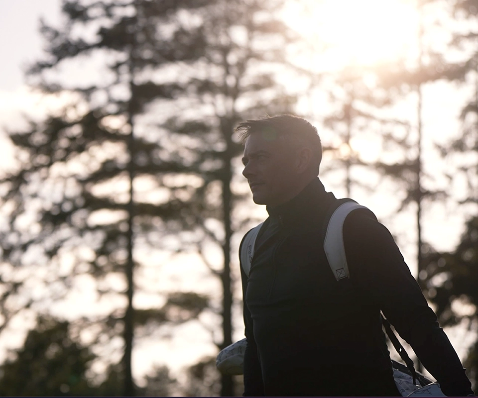 Male golfer carrying his clubs at sunset