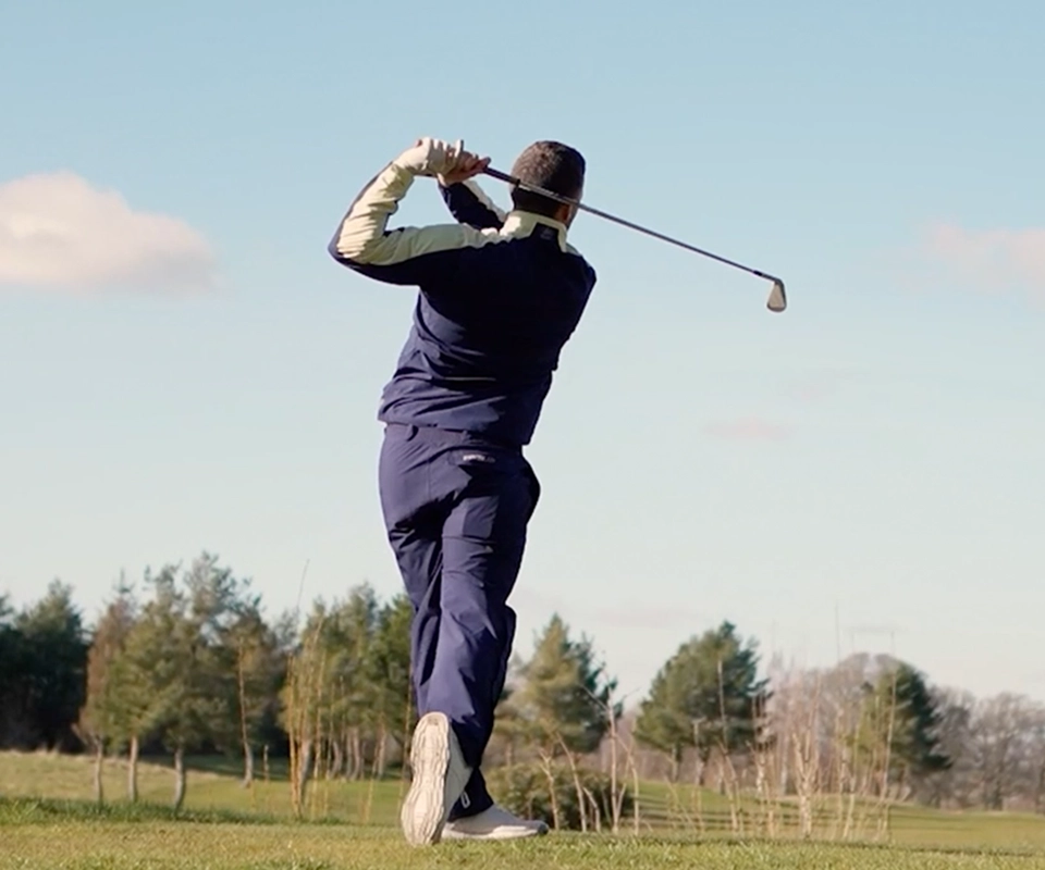 Golfer swinging a club with his back to the camera on a sunny day